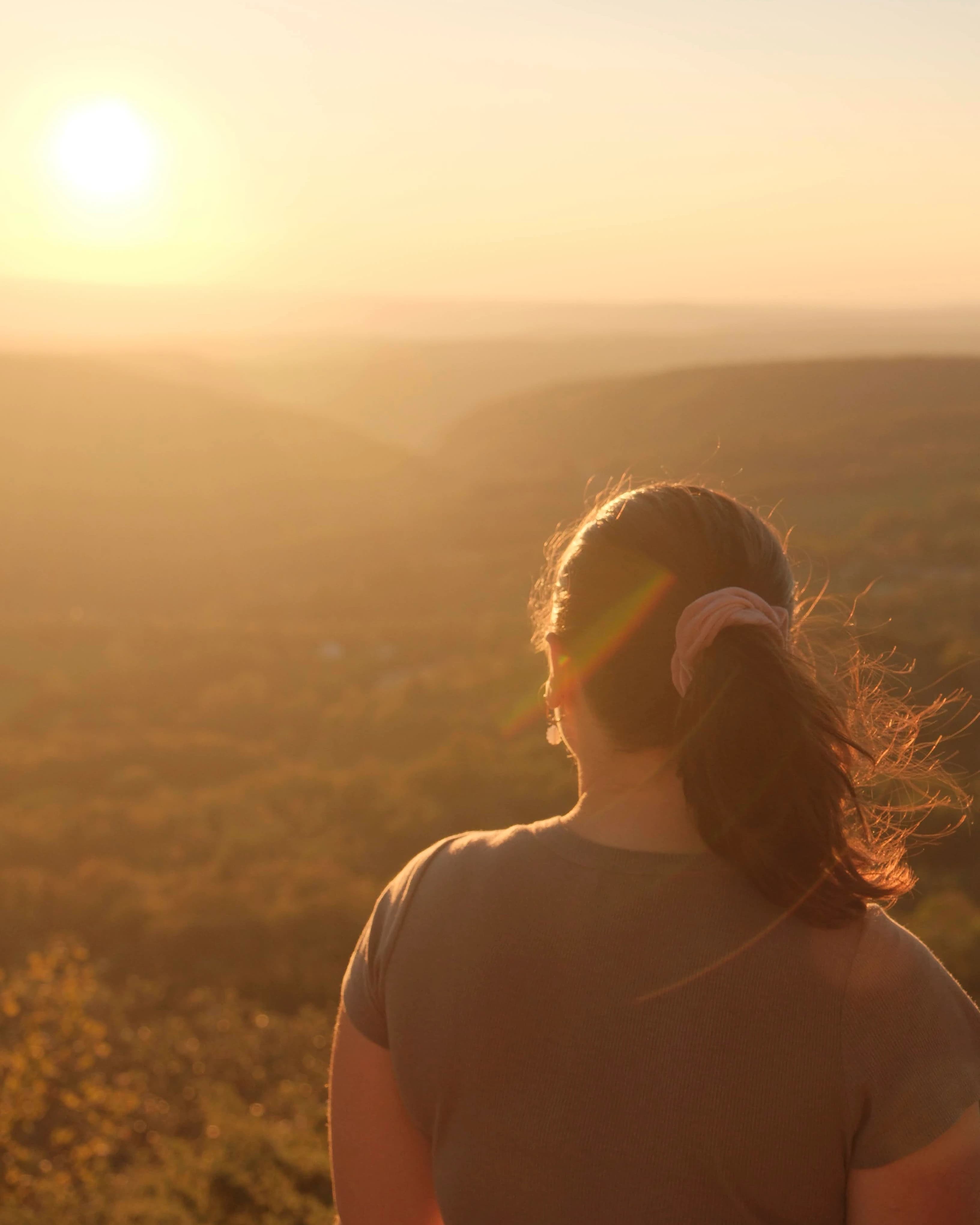 Persoon die bij zonsondergang uitkijkt over een heuvelachtig landschap